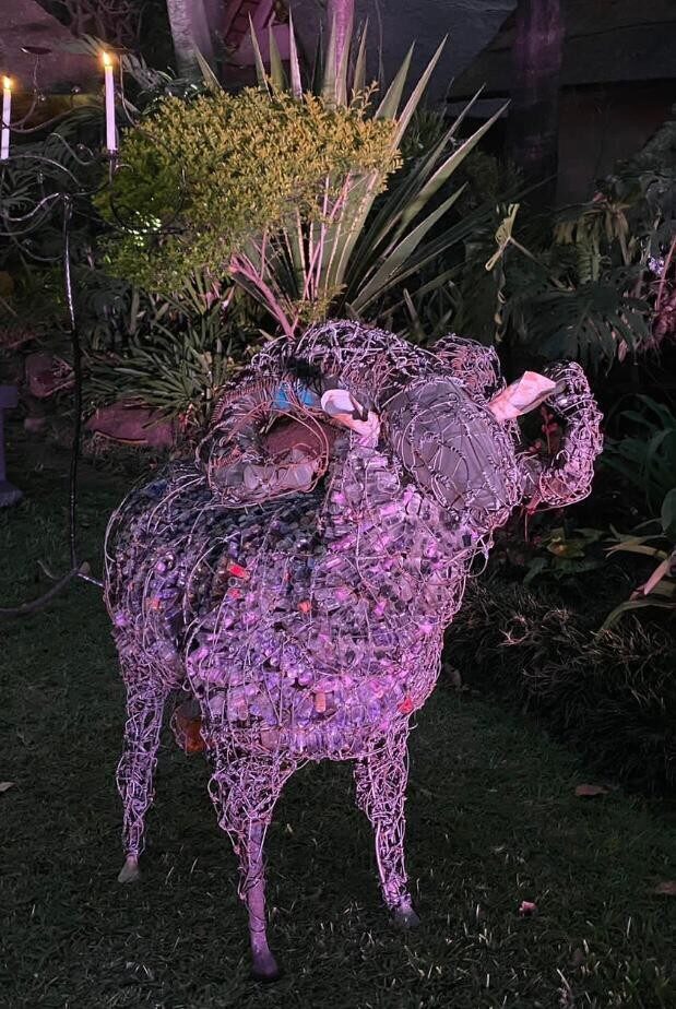 Bighorn sculpture standing in a garden, lit at night