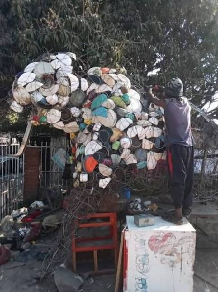 The artist on a ladder building a large elephant head from wire and caps